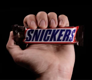 Hand holding a Snickers chocolate bar against a black background