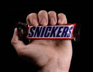 Hand holding a Snickers chocolate bar against a black background